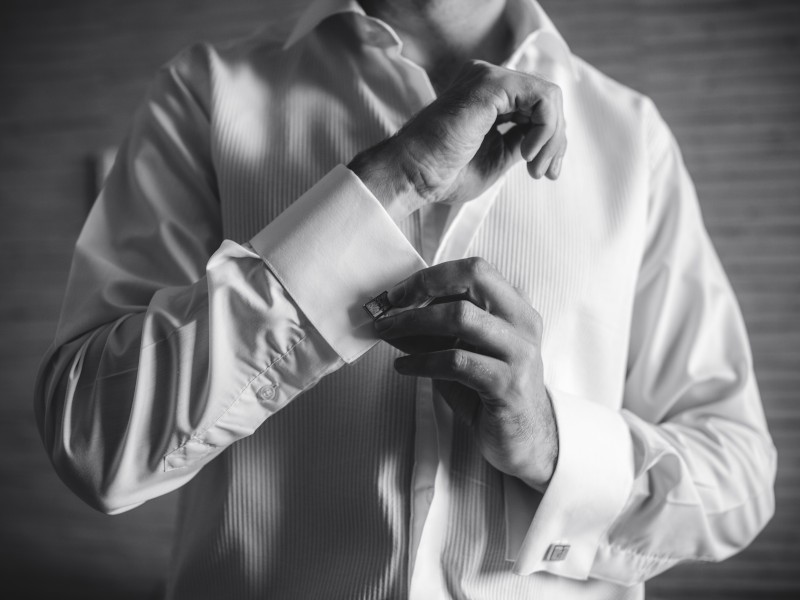 a black and white photo of a groom putting on cufflinks