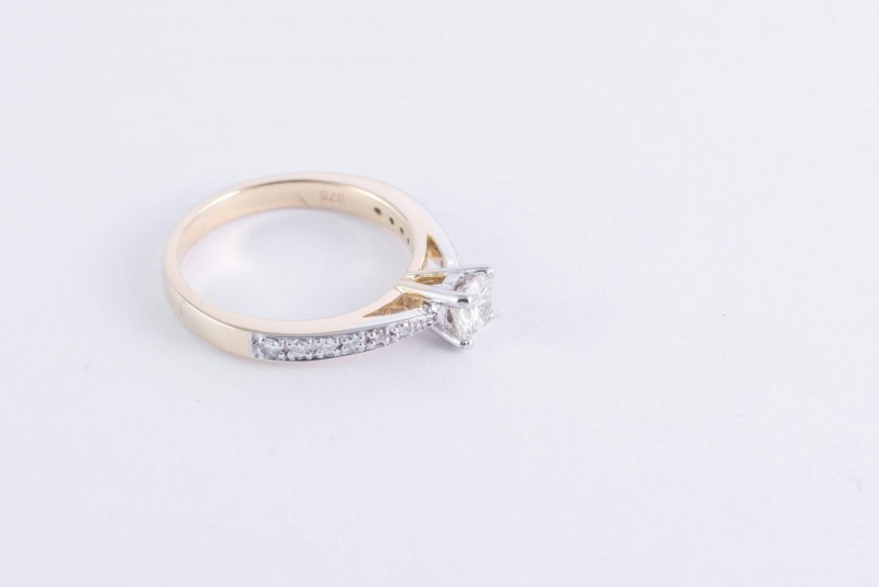 yellow gold diamond solitaire ring with diamond set shoulders on a white background