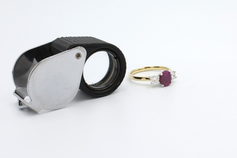 a jewellers magnifying glass next to a ruby and gold engagement ring