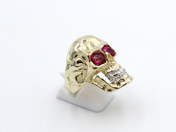 right view of a large gold skullr ing with red ruby eyes