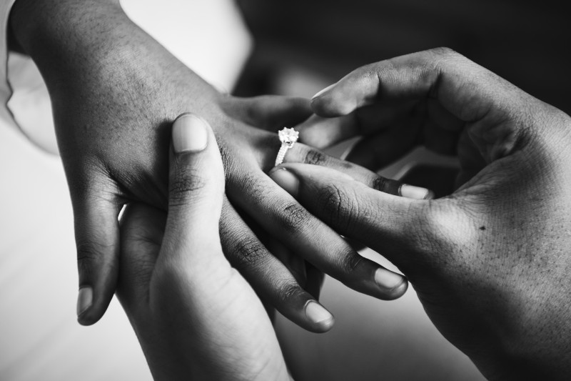 black white photo man putting engagement ring on woman's hands