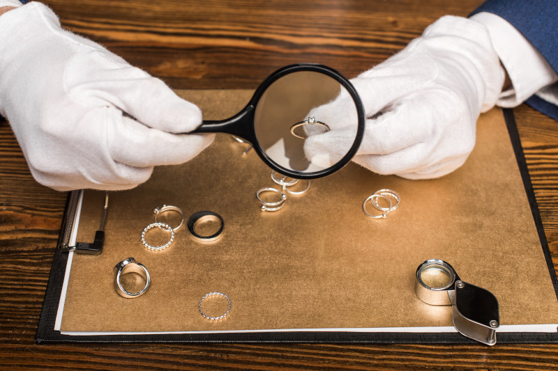 A jeweller inspecting different types of rings with a magnifying glass.