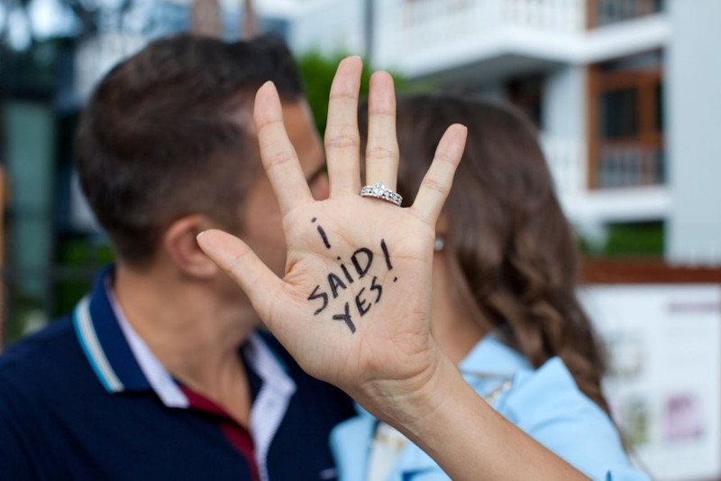 newly engaged couple kissing with the woman holding her hand up with the message I said yes written on it